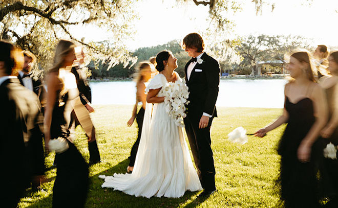 The bride and groom take photos with the wedding party as they walk fast past them. 