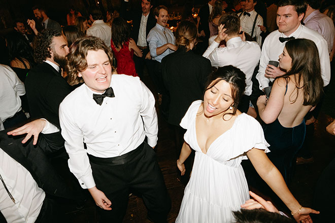 The bride and groom singing and dancing at the reception on the dance floor with guests. 