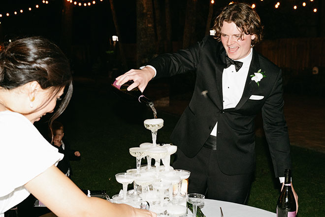 The groom happily pours the champagne on the tower of glasses. 