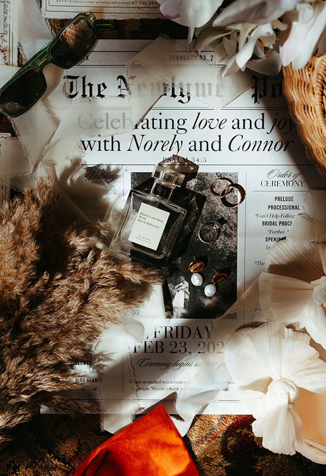 The couple's invite layout reads their wedding date as a newspaper with her perfume and rings lay on top. 