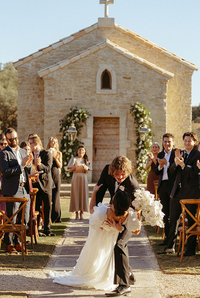 The bride and groom make their way down after saying their "i do's" and kiss at the end with the church view behind them. 