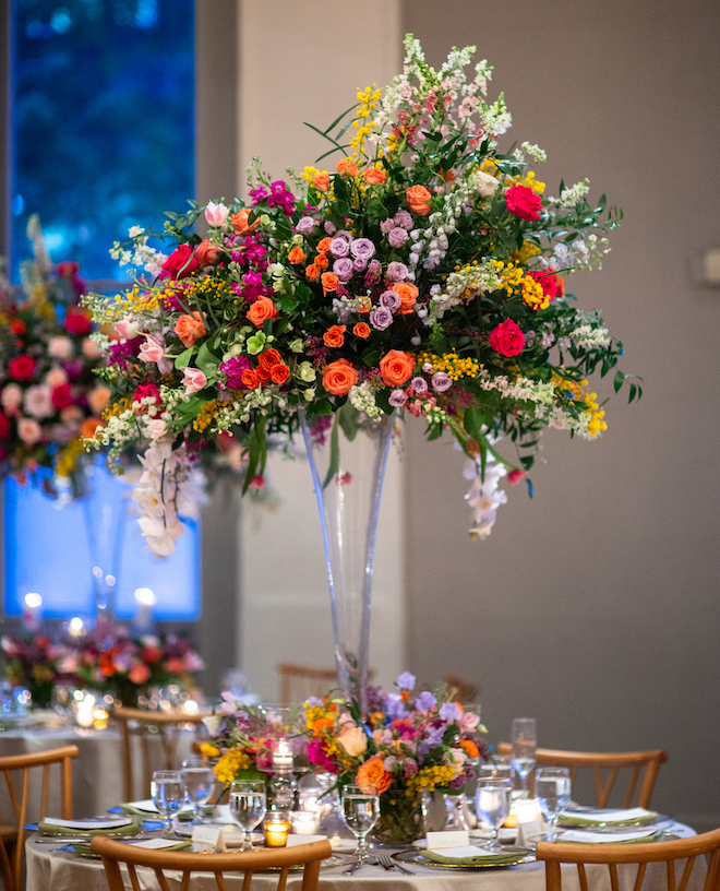 A large floral centerpiece made of greenery, red, orange and purple florals. 