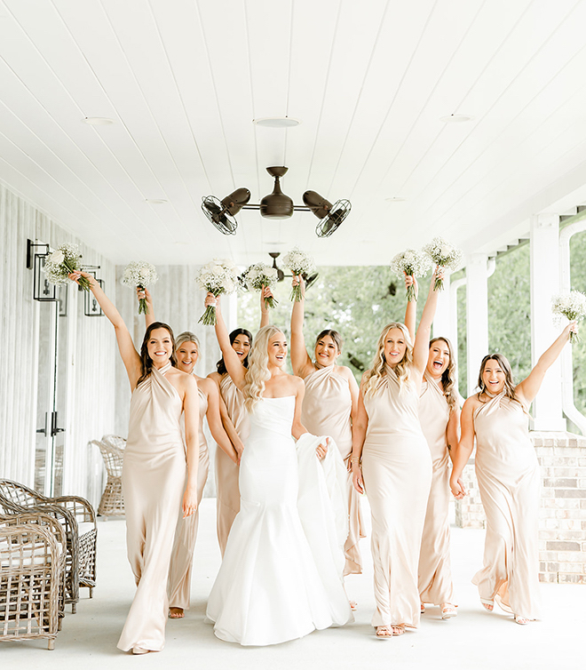 The bride and her bridesmaids pose for a photo with their bouqets in the air. 