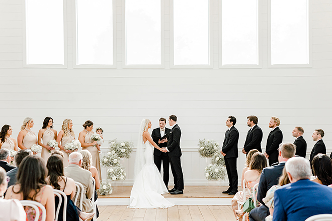 The bride and groom stand at the end of the alter holding hands. 