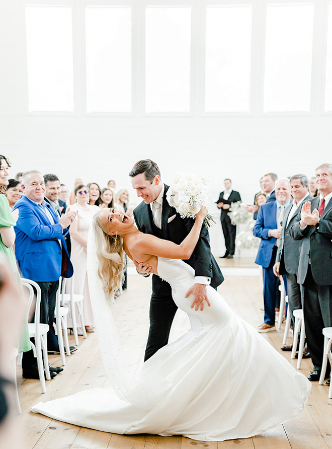 The groom dips the bride at the end of the aisle with smiles on their faces. 