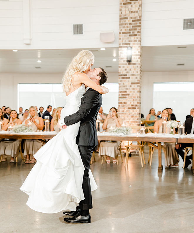 The groom is holding the bride in his arms at the wedding reception during the first dance. 