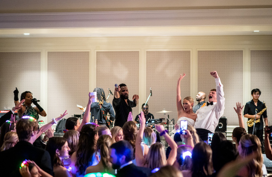 Bride and groom stand on the stage at their reception, dancing and singing with the band in front of the crowd with guests. 