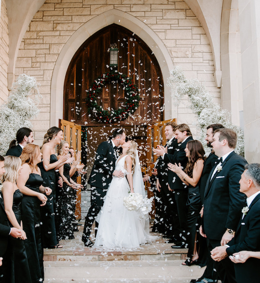 Bride and groom leaving their wedding ceremony while the bridal party throws confetti in the hair as they kiss. 