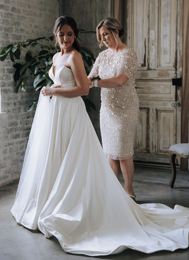 The mother of the bride helps her daughter put on her wedding gown. 