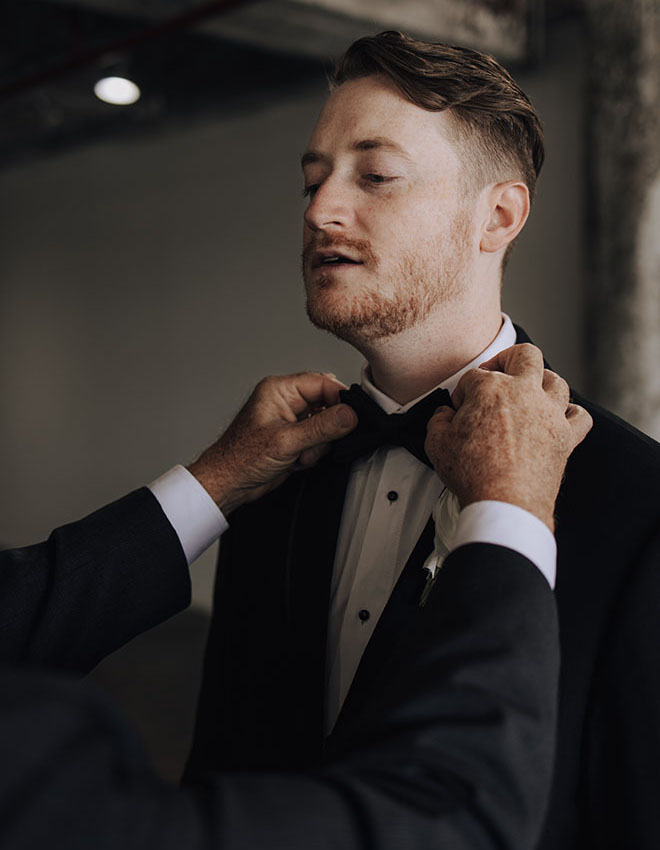 A family member helps the groom adjust his bow tie. 