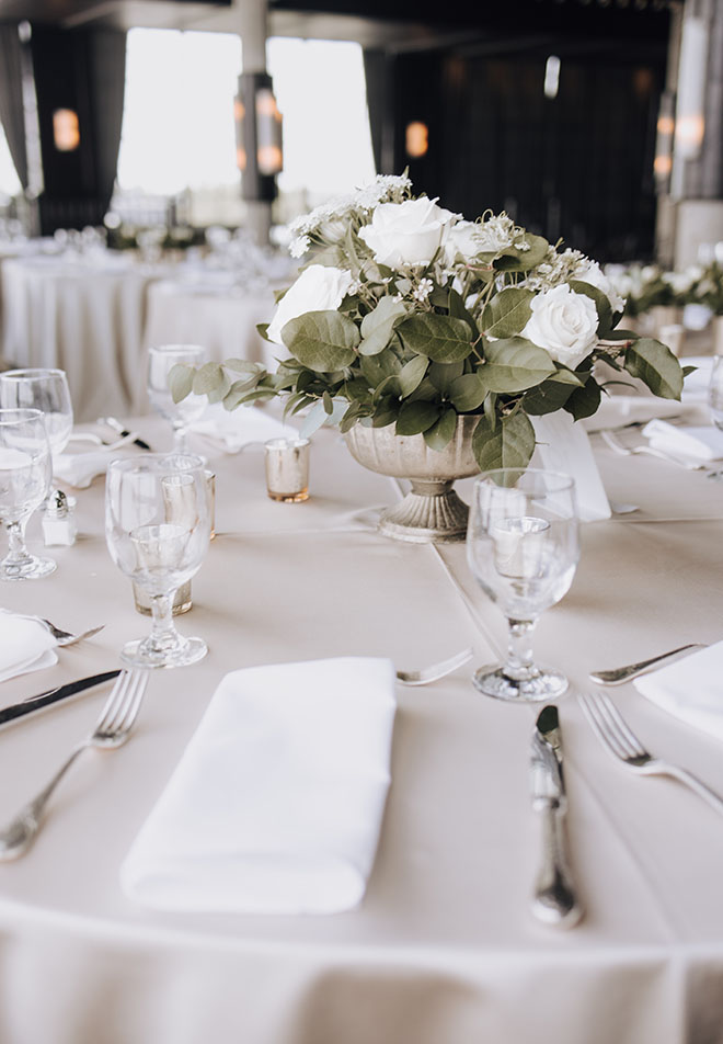 White roses and greenery decorate the reception tables at the neutral-toned wedding.