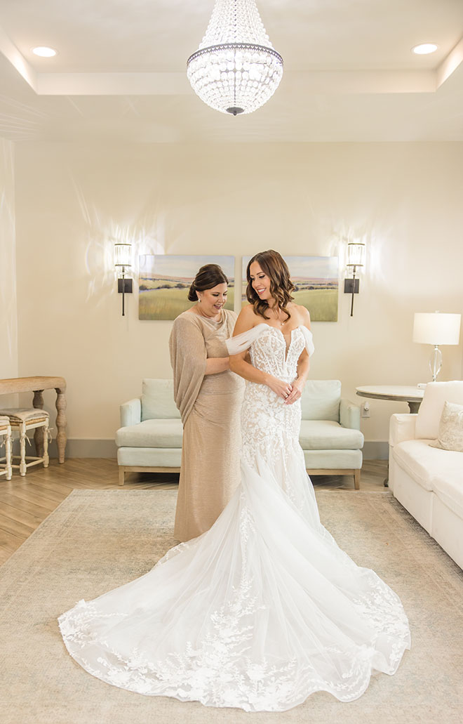 The mother of the bride helps adjust her daughters wedding dress.