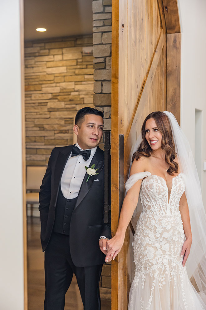 A sliding door seperates the bride and groom while they hold hands.