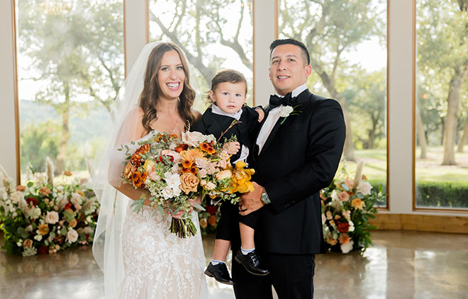 The bride and groom smile with their son at their wedding ceremony.