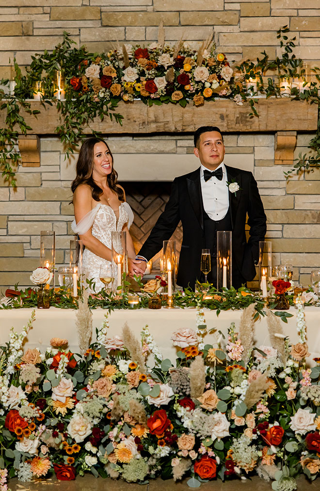 The bride and groom hold hands surrounded by autumn-inspired wedding florals.