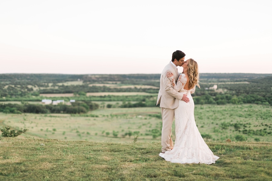 A couple kisses as they pose for a photo with a backdrop of Fredericksburg, Texas. 