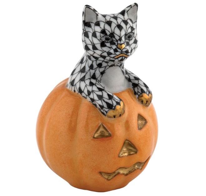 A figurine of a black and white cat sitting in an orange jack-o-lantern. 