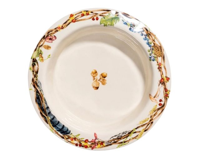 A plate with fall foliage on the rim of the plate with acorns in the center. 