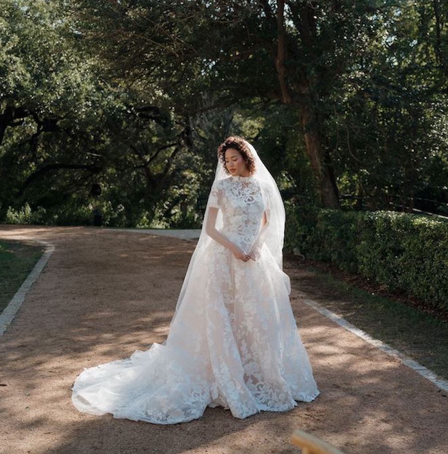 Bride looks stunning in her lace short-sleeve wedding dress and veil as she stands in lush greenery. 