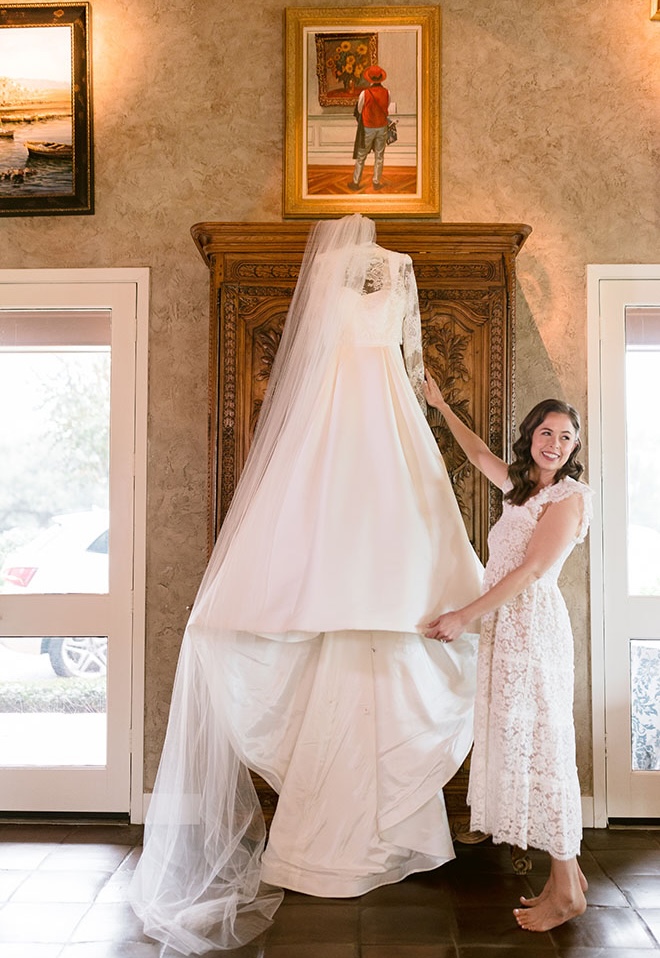 The bride smiles next to her wedding gown that hangs from an armoire in her childhood home. 