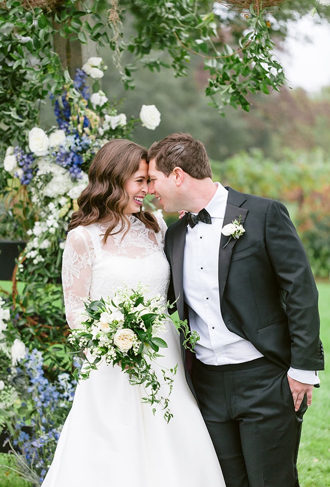 The bride and groom smile at each other while standing under a blue and white floral arch. 