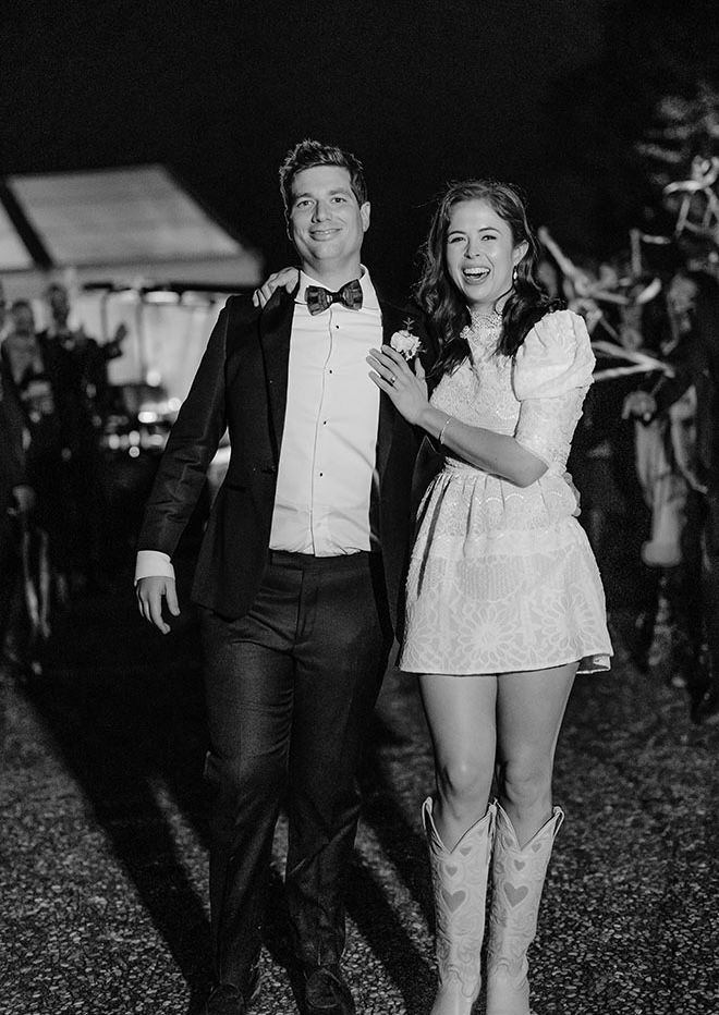 The bride and groom exit their wedding reception as guests celebrate with streamers. 