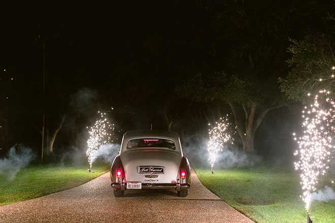 The bride and groom ride off in a silver vintage car from their outdoor tented wedding.