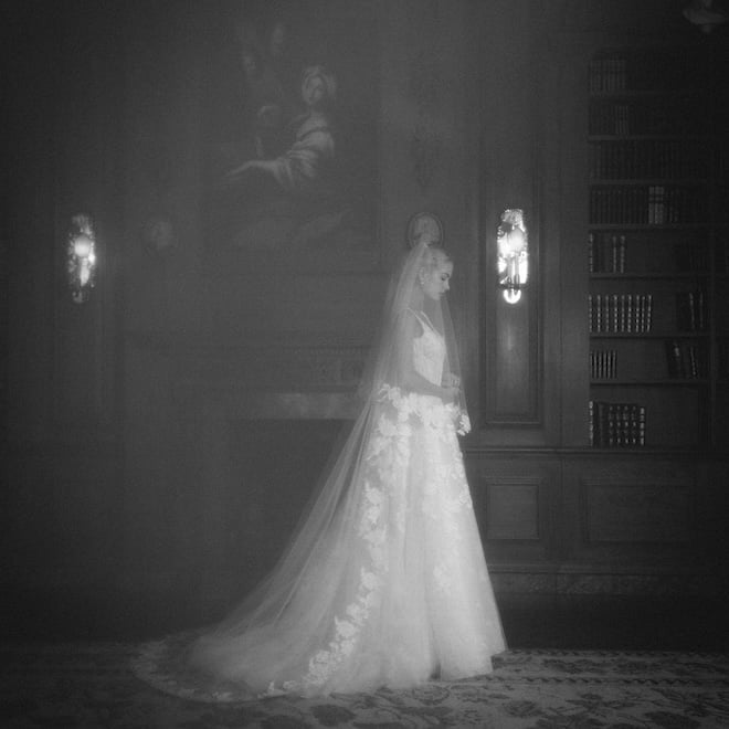 Black-and-white photo of A bride wearing the Anne Barge Oakland gown features a scoop neck A-line silhouette with a low back adorned with intricate floral embroidery and a cathedral length veil with vine-embroidery on the trim.