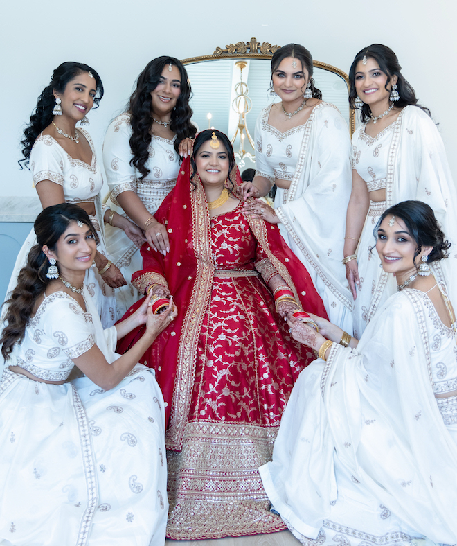 The bride wearing red with her bridesmaids surrounding her wearing white. 