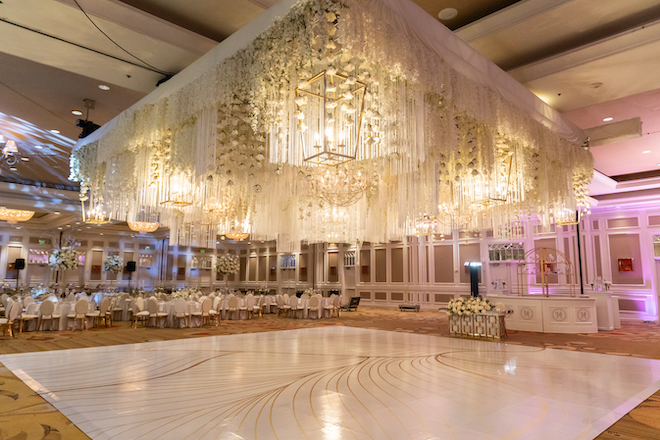 The reception at Houston Marriott Sugar Land with a white floral canopy and a white and gold dance floor. 