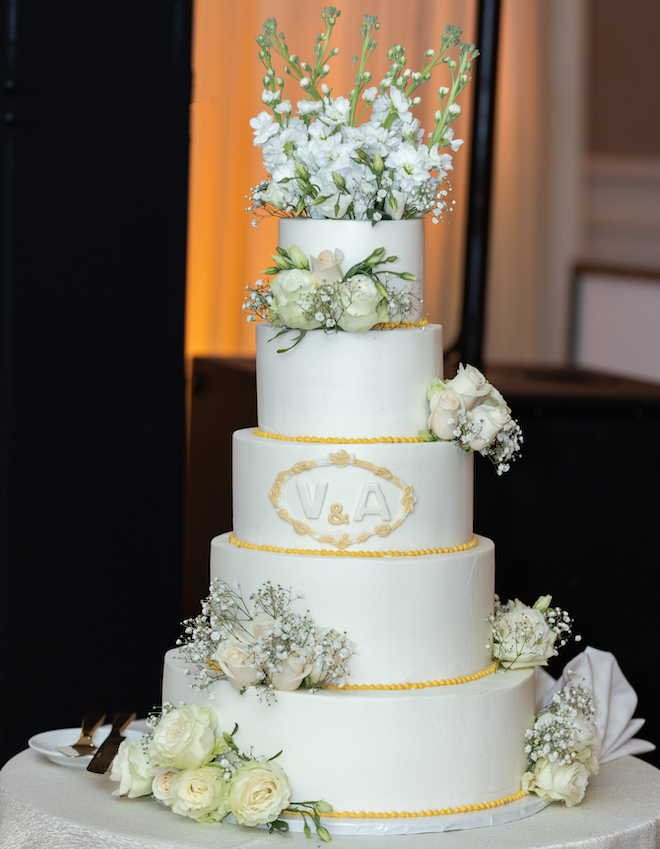 A five-tier white cake garnished with white florals. 