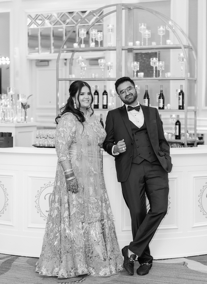 A black and white photo of the bride and groom smiling at the bar of their wedding reception. 