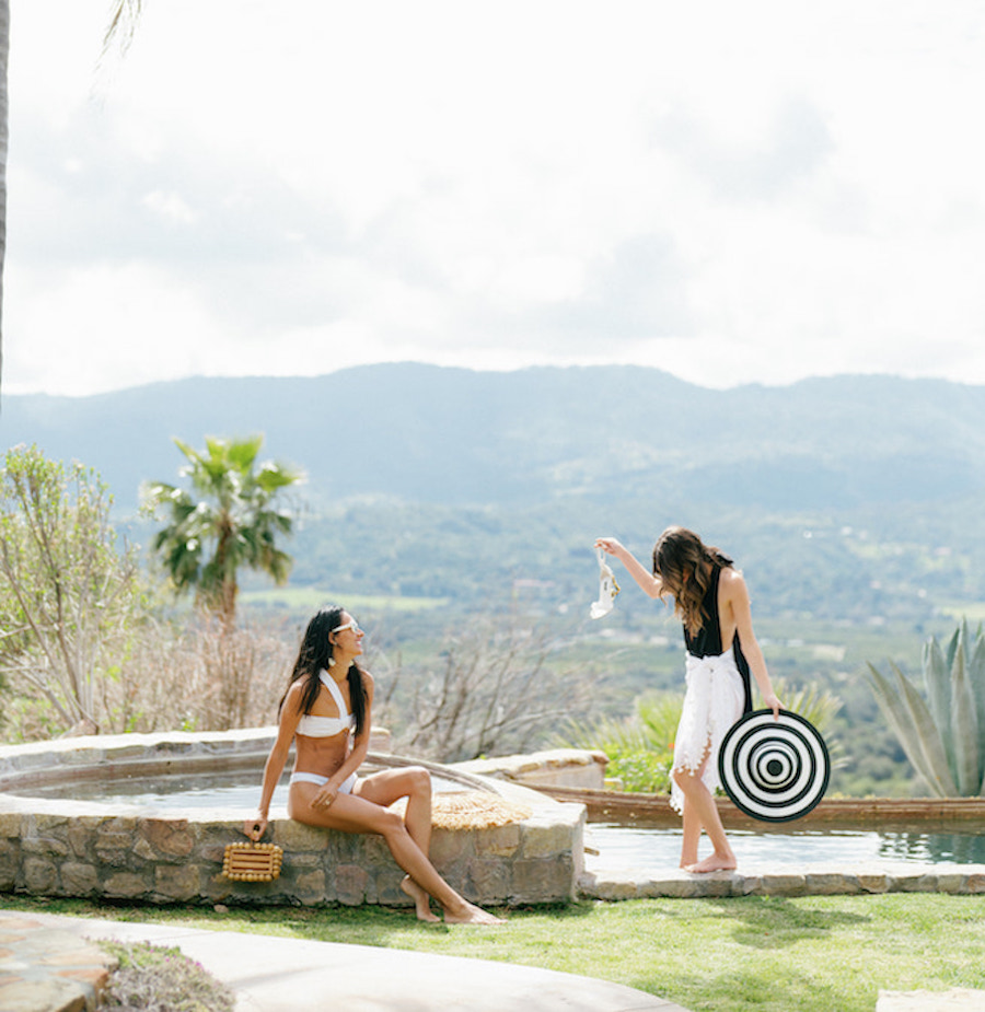 Girls standing by the pool with a breath taking background dressed for the pool and tanning in the sun. 