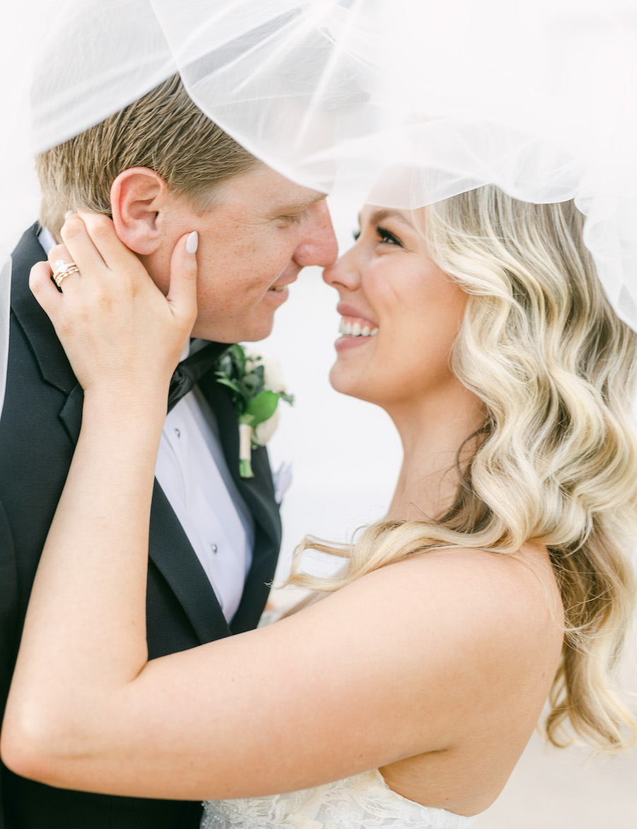 The bride and groom pose for photos, while the bride wears a gown along with a veil and the groom wears a suit. 