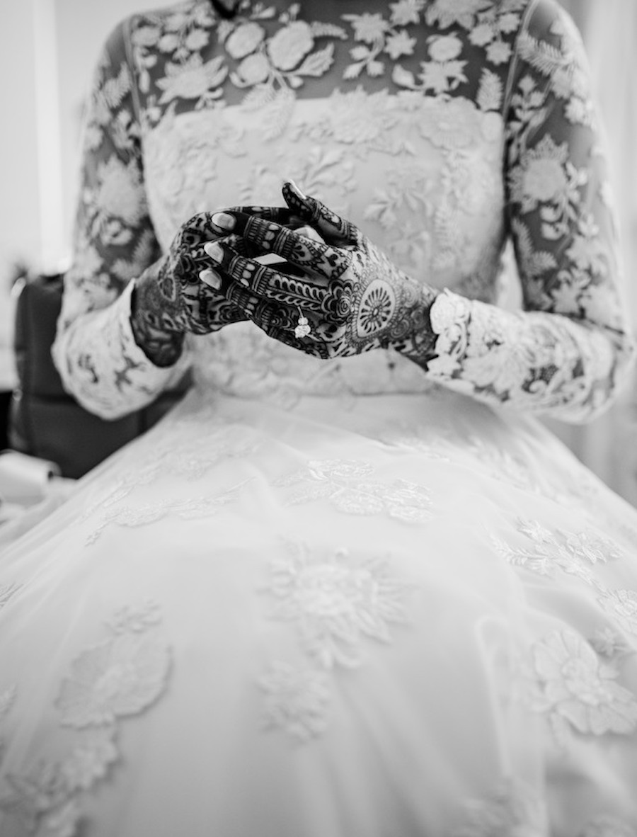 A bride wears her long sleeve, lace wedding gown with her double diamond engagement ring and henna. 