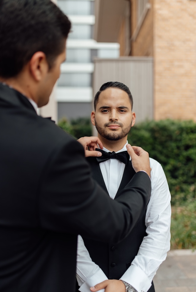 A groomsmen helps the groom adjust his bow tie.