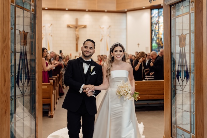 The bride and groom walk out of their traditional church ceremony holding hands.