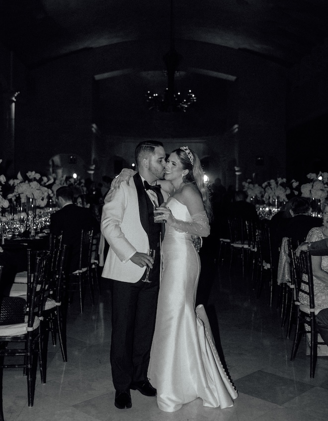 The groom kisses the bride on her cheek at their black and white wedding reception.