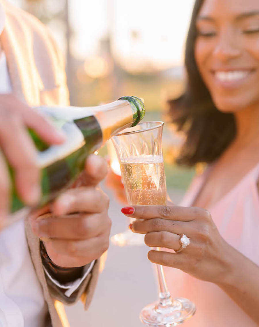 Bride poses with a glass of champagne with her fiance as they celebrate their engagement. 