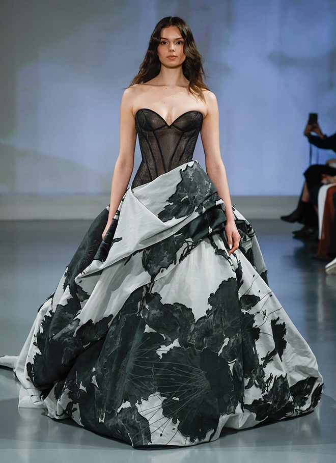 The model walks down the runway wearing a black and grey floral printed gown. 