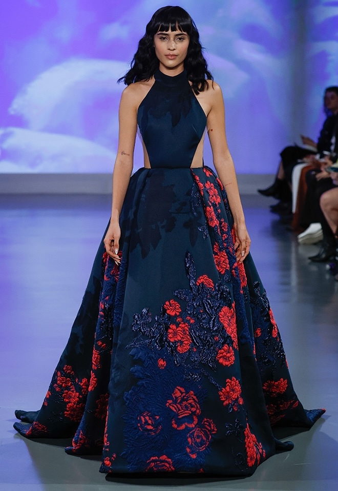 The model walks down the runway wearing a dark colored wedding dress with red florals by Ines Di Santo. 