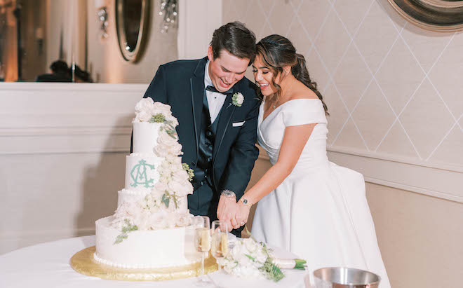 The bride and groom cut their four-tier white wedding cake. 