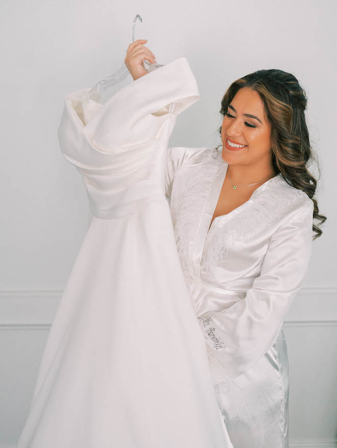 The bride smiles while holding her wedding dress before she gets married. 