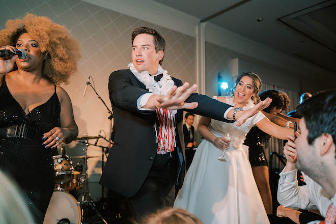 Guests along with the bride and groom dance to live music at their wedding reception with their hands in the air. 