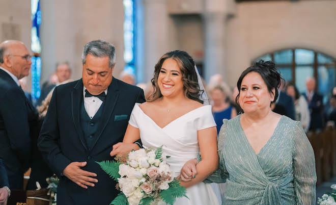 The bride walks down the aisle with her parents by her side. 