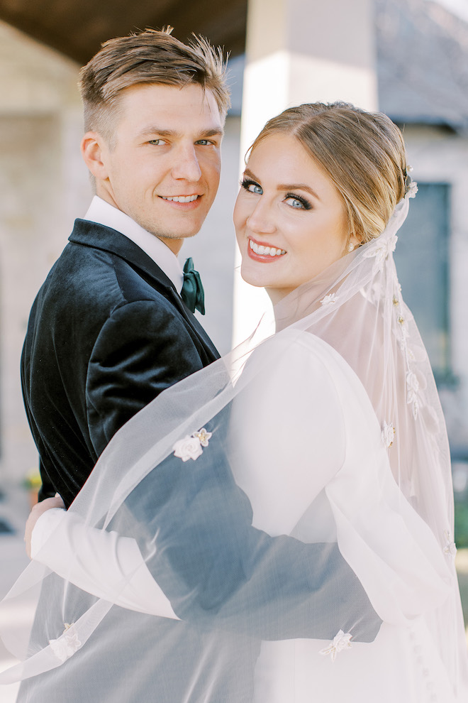 A bride and groom look and the camera while hugging during a sunlit hill country wedding styled shoot at Cricket Hill Ranch in Dripping Springs, TX.