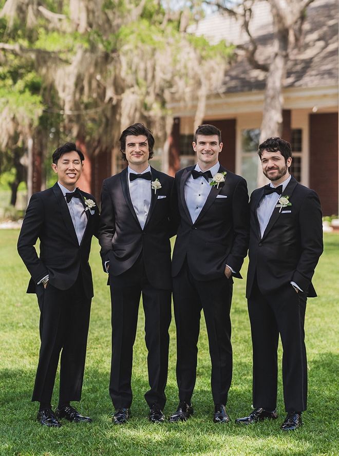 The groom and his groomsmen stand outside their countryside wedding venue.