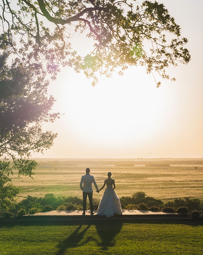 The bride and groom hold has as they look off into the sunset overlooking the Texas Hill Country.