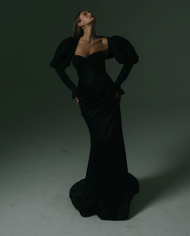 The model wears a dark-colored wedding dress by Hera Couture.