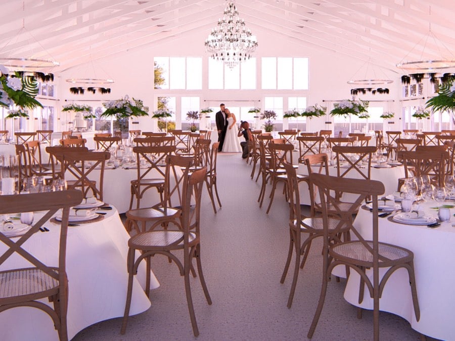 A ballroom venue space with white decorations and a chandelier above reception dinner tables.